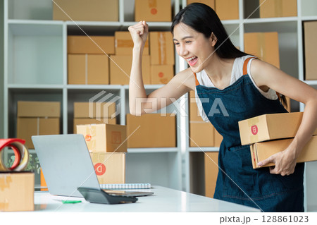 Enthusiastic Entrepreneur Celebrating Online Business Success with Packages and Laptop in Modern Office Enthusiastic Entrepreneur Celebrating Online Business Success with Packages and Laptop in Modern Office 128861023