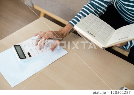 Person Using Calculator and Reading Book at Desk for Financial Planning and Budgeting Person Using Calculator and Reading Book at Desk for Financial Planning and Budgeting 128861287
