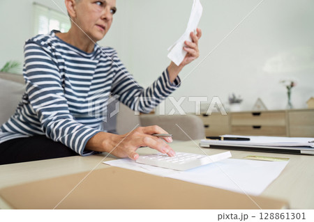 Senior Woman Managing Finances at Home with Calculator and Documents in Living Room Senior Woman Managing Finances at Home with Calculator and Documents in Living Room 128861301