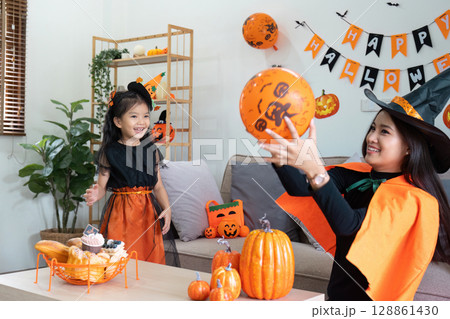 Mother and Daughter Celebrating Halloween at Home with Costumes, Decorations, and Pumpkin-Themed Activities Mother and Daughter Celebrating Halloween at Home with Costumes, Decorations, and Pumpkin-Themed Activities 128861430