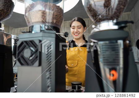 Barista in Yellow Apron Smiling While Preparing Coffee in a Modern Cafe with Professional Equipment 128861492