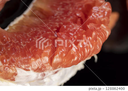 red citrus on the table, peeled citrus grapefruit with bright red and juicy flesh, the fruit is reflected on a black mirror surface 128862400