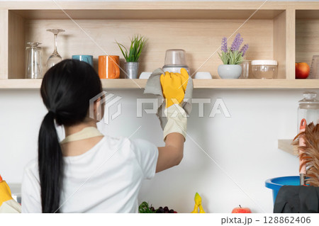 Shelf Cleaning. Woman dusting shelves in a tidy kitchen environment. Shelf Cleaning. Woman dusting shelves in a tidy kitchen environment. 128862406