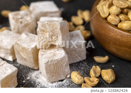 Turkish delight in sugar with nuts , scattered oriental sweets Turkish delight with peanuts on a black board, close up, side view Turkish delight in sugar with nuts , scattered oriental sweets Turkish delight with peanuts on a black board, close up, side view 128862426