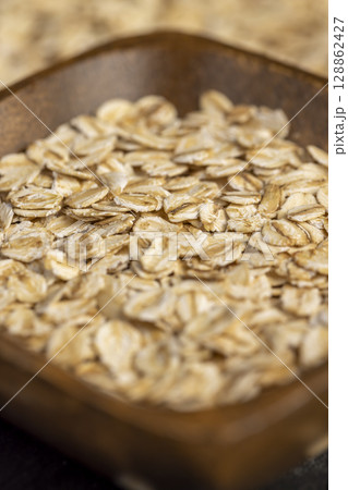 oat flakes into a square-shaped wooden bowl, oatmeal for quick cooking of porridge , closeup, side view oat flakes into a square-shaped wooden bowl, oatmeal for quick cooking of porridge , closeup, side view 128862427