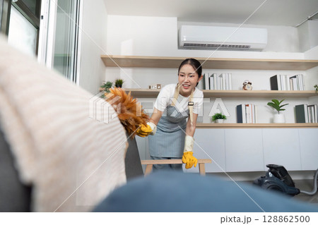Home Cleaning. Woman using duster to clean furniture in stylish living area. Home Cleaning. Woman using duster to clean furniture in stylish living area. 128862500