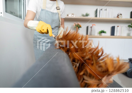 Home Cleaning. Woman cleaning sofa with duster in modern living room. Home Cleaning. Woman cleaning sofa with duster in modern living room. 128862510