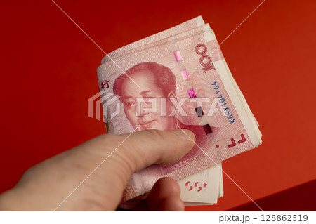 holding a large stack of Chinese yuan in his hand on a red background, holding a large amount of money in yuan in the hands of a man 128862519