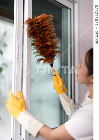 Home Cleaning. Woman dusting window with duster in modern interior. Home Cleaning. Woman dusting window with duster in modern interior. 128862579