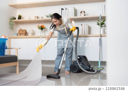 Home Cleaning. Young woman vacuuming the floor with focus and care. 128862586