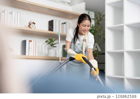 Home Cleaning. Joyful woman vacuuming while listening to music in a modern living room. Home Cleaning. Joyful woman vacuuming while listening to music in a modern living room. 128862588