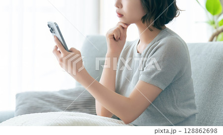 スマートフォンを見ながら考えごとをする女性 128862698