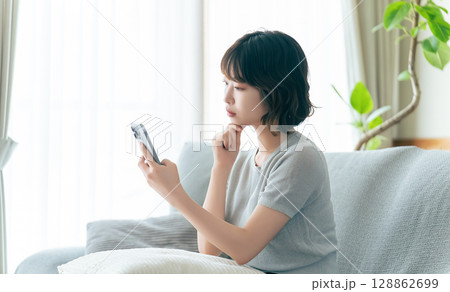 スマートフォンを見ながら考えごとをする女性 128862699