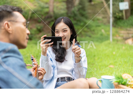 Outdoor Fun. Young woman capturing joyful moment with smartphone in nature. Outdoor Fun. Young woman capturing joyful moment with smartphone in nature. 128864274