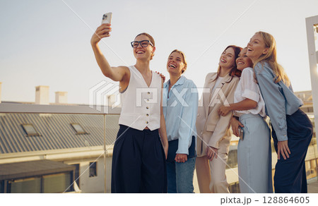 A group of friends joyfully taking a selfie together on the vibrant city rooftop during daytime 128864605
