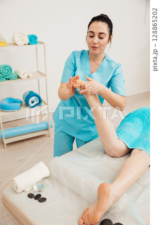 Masseur doing medical foot massage to woman Masseur doing medical foot massage to woman 128865202