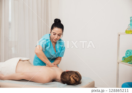 Massage therapist doing medical back and body massage to woman Massage therapist doing medical back and body massage to woman 128865211