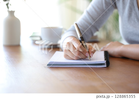 Woman hand writing with a pen on notebook on a table Woman hand writing with a pen on notebook on a table 128865355