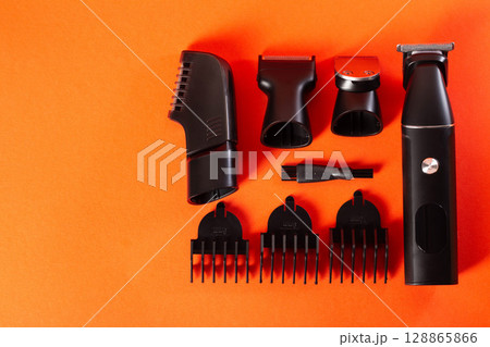 A set of trimmer for a haircut and different attachments for it on a red background. Barbershop and hair salon services. Copy space for text 128865866