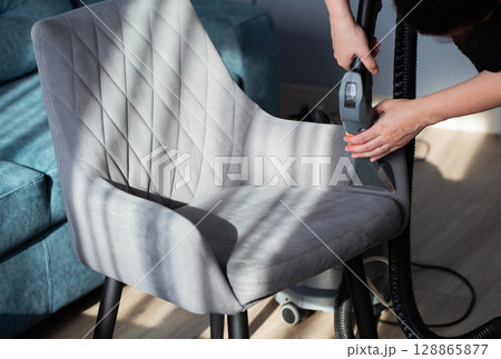 Cleaning the upholstery of a gray chair from dirt with a washing vacuum cleaner. Cleaning services, close-up. Industry 128865877