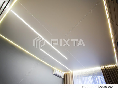 Beautiful modern stretch ceiling with yellow LED lines around the perimeter. Designer stylish ceiling in the hall. Beautiful modern stretch ceiling with yellow LED lines around the perimeter. Designer stylish ceiling in the hall. 128865921
