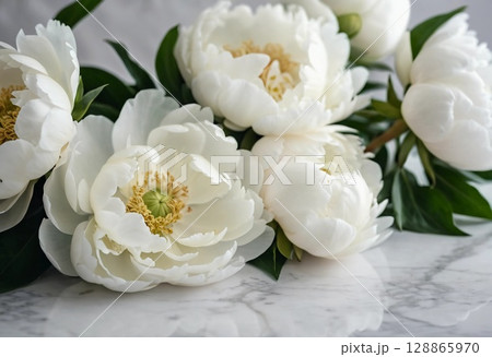 Delicate white peonies rest gracefully on a smooth marble surface, their soft petals unfurling amidst lush green leaves, illuminated by gentle natural light Generative AI 128865970