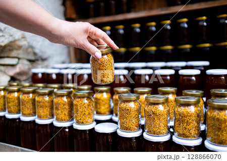 Hand selecting honey jars from shelf filled with bottled honey and bee pollen 128866070