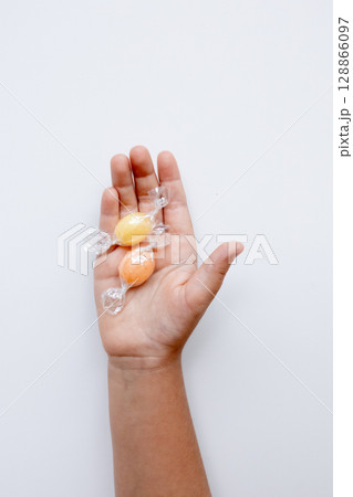 Child hand holding wrapped candy in a caucasian young hand on white background 128866097