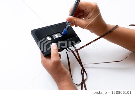 Hands repairing audio cassette tape with pen on white background 128866101