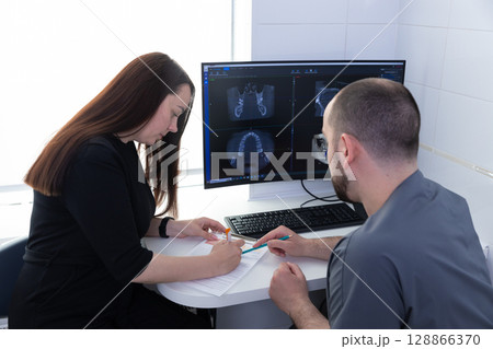 A Professional Consultation on Dental Health: A Patient Discusses Treatment with a Dentist While Reviewing X-ray Results on a Computer Screen 128866370