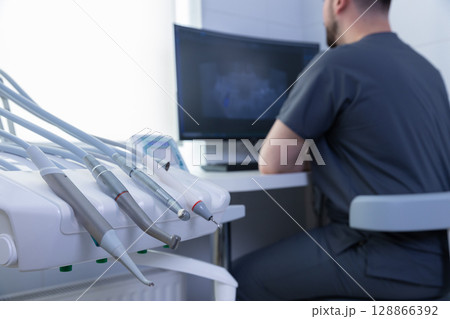 A Focused Dentist at Work in a Modern Dental Office with State-of-the-Art Equipment and a Computer Monitor Displaying Patient X-rays for Diagnosis and Treatment Planning A Focused Dentist at Work in a Modern Dental Office with State-of-the-Art Equipment and a Computer Monitor Displaying Patient X-rays for Diagnosis and Treatment Planning 128866392