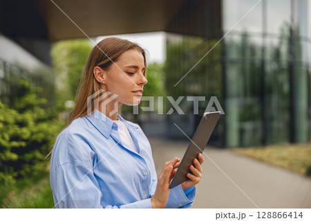 A young woman is utilizing a tablet device in a stylish modern outdoor environment 128866414