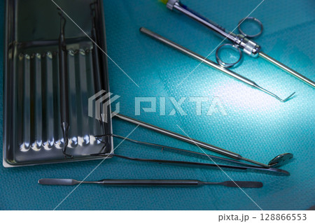 A Close-Up View of Surgical Instruments on a Blue Surgical Drape with Glare Highlighting Their Steel Surface and Reflected Smoothness in a Medical Environment Setup A Close-Up View of Surgical Instruments on a Blue Surgical Drape with Glare Highlighting Their Steel Surface and Reflected Smoothness in a Medical Environment Setup 128866553