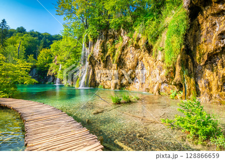 Wooden footpath at Plitvice national park, Croatia. Pathway in the forest near the lake and waterfall. Fresh beautiful nature, peaceful place. Famous tourist destination. Wooden footpath at Plitvice national park, Croatia. Pathway in the forest near the lake and waterfall. Fresh beautiful nature, peaceful place. Famous tourist destination. 128866659
