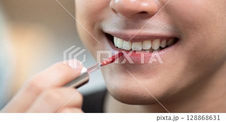 Beauty Routine. Male applying red lip gloss for a stylish look. Beauty Routine. Male applying red lip gloss for a stylish look. 128868631