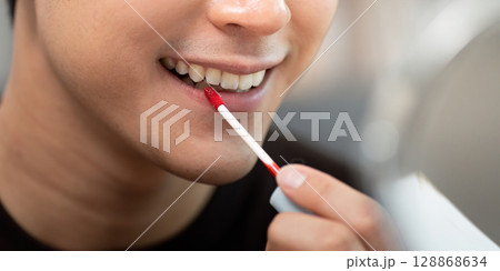 Grooming. Young man applying red lip gloss with precision. 128868634