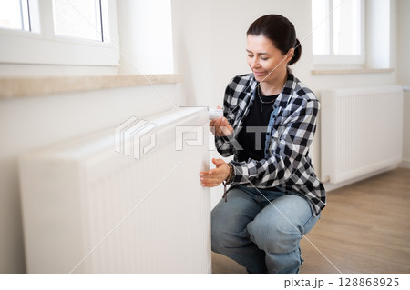 Woman Checks The Temperature And Adjusts The Heater At Home 128868925