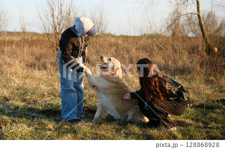 Girls Asking Adorable Golden Retriever Dog To Give A Paw Outdoors 128868928