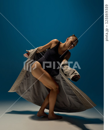 Young woman bending in dramatic spotlight with trench coat and emotional movement in contemporary dance 128869389