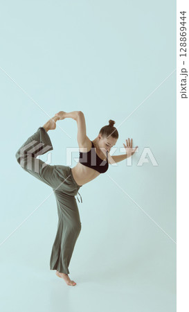 Contemporary dancer balancing in standing pose with focused expression against pale background 128869444