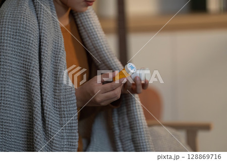 Health and Wellness. Woman holding medication bottle, wrapped in cozy blanket. Health and Wellness. Woman holding medication bottle, wrapped in cozy blanket. 128869716