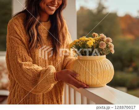 A young woman stands on a cozy autumn porch holding a seasonal bouquet. A young woman stands on a cozy autumn porch holding a seasonal bouquet. 128870017