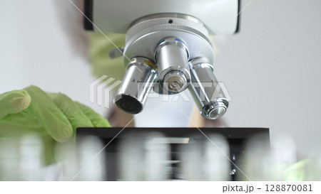 Close up of green gloved hands of a scientist adjusting a microscope in a laboratory, emphasizing the significance of scientific research and analysis. Medicine, healthcare and science concept Close up of green gloved hands of a scientist adjusting a microscope in a laboratory, emphasizing the significance of scientific research and analysis. Medicine, healthcare and science concept 128870081