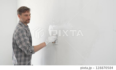 Construction worker spreading plaster on white wall, wearing protective gloves and t-shirt during home renovation project, working with professional skill and focus Construction worker spreading plaster on white wall, wearing protective gloves and t-shirt during home renovation project, working with professional skill and focus 128870584