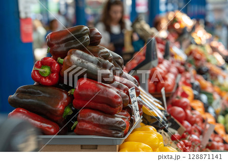 Raw juicy red bell pepper and vegetables on display at a food market. Selective focus on sweet pepper. Paprika 128871141