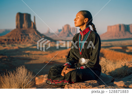 A woman sits on a rock in the desert, wearing a black dress and a head scarf A woman sits on a rock in the desert, wearing a black dress and a head scarf 128871883