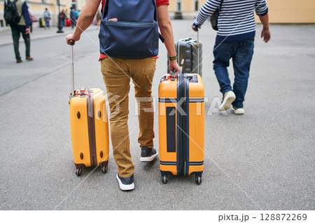 Tourists walking with luggage toward city 128872269