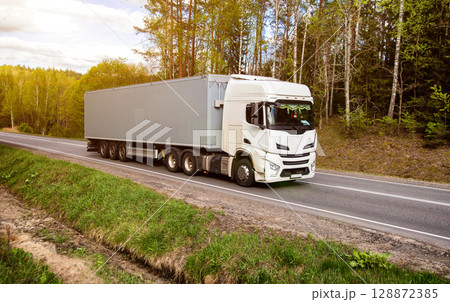 Modern truck transports cargo against the backdrop of forest and sun in summer, beautiful sky with clouds. Logistics company delivering cargo on international routes. Copy space for text. Freight Modern truck transports cargo against the backdrop of forest and sun in summer, beautiful sky with clouds. Logistics company delivering cargo on international routes. Copy space for text. Freight 128872385