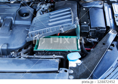 Old dirty air filter in the underhood space of the car. Car maintenance, close-up 128872452