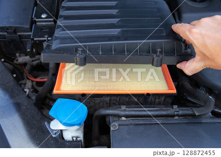 Installing a new clean air filter in the engine compartment of a car to clean the air in the car engine, close-up Installing a new clean air filter in the engine compartment of a car to clean the air in the car engine, close-up 128872455
